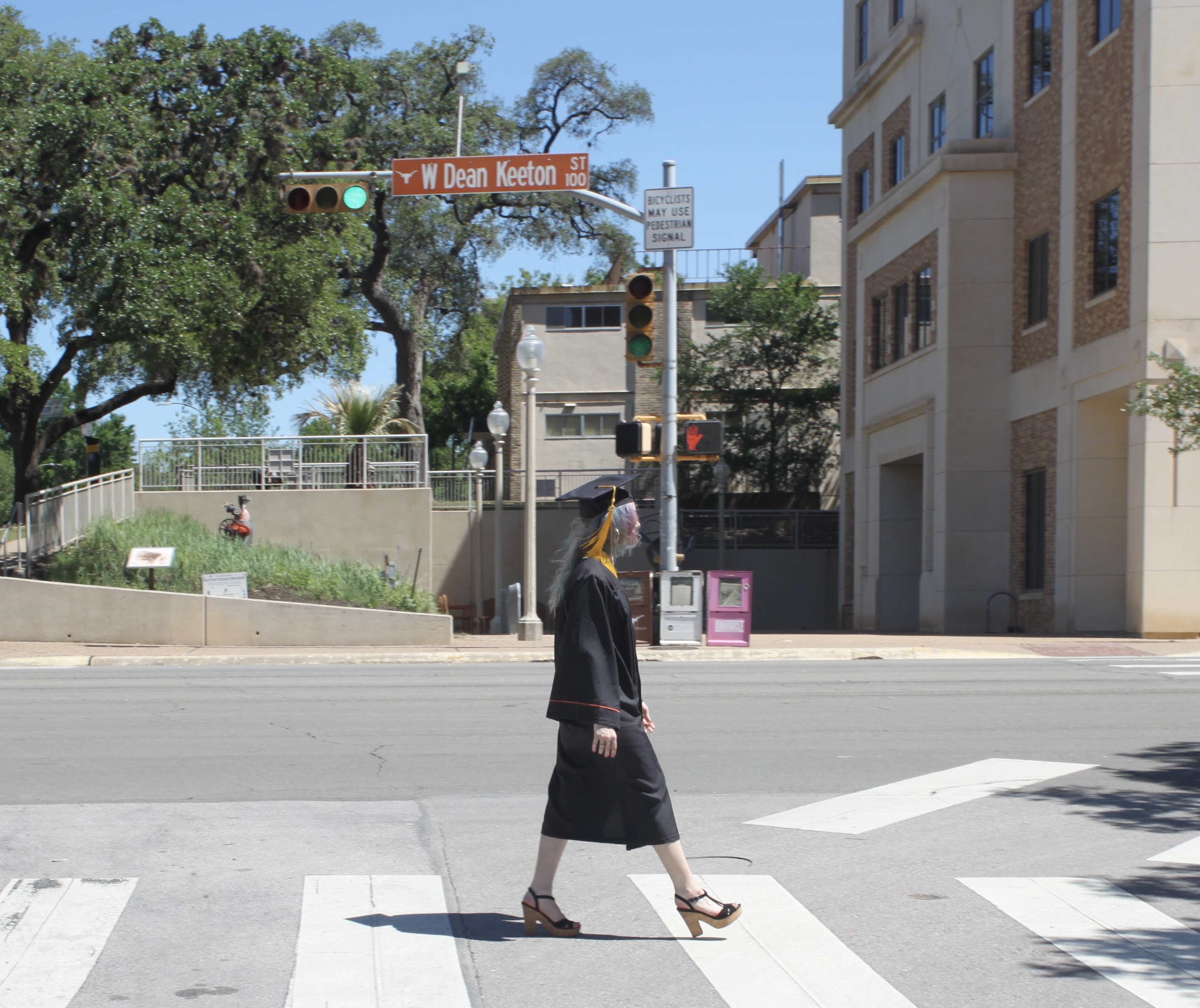 Kiersten walking across Dean Keeton St. in her cap and gown